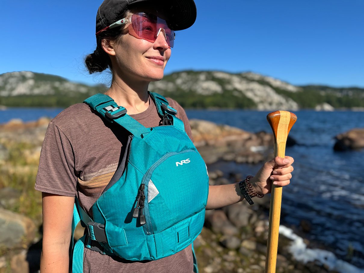 Kaydi Pyette wearing the NRS Ninja PFD while standing on a shoreline with paddle in hand