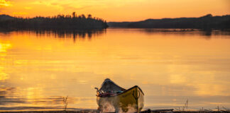 a campfire with canoe beached behind it at dusk