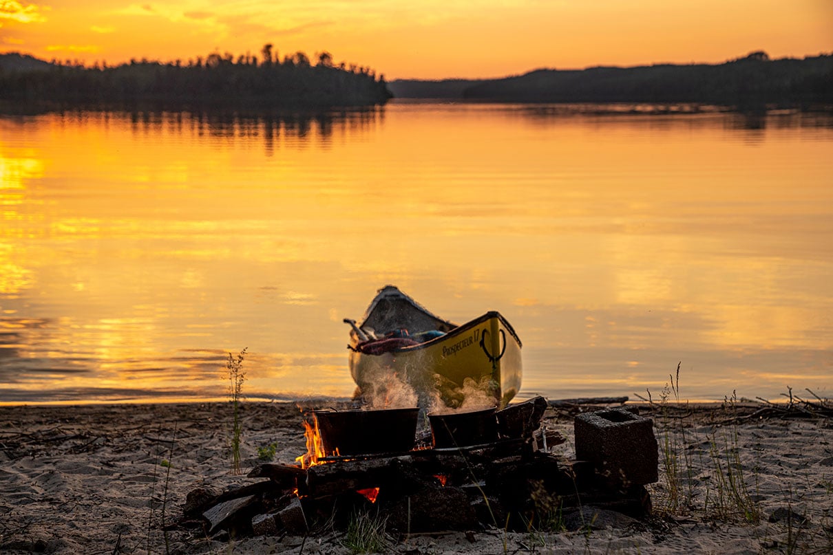 a campfire with canoe beached behind it at dusk