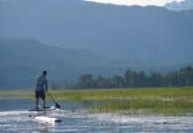 man standup paddleboarding in front of a scenic mountain landscape