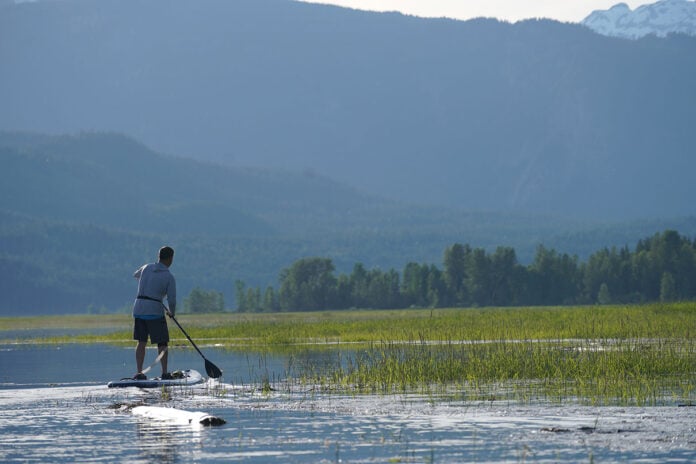 man standup paddleboarding in front of a scenic mountain landscape