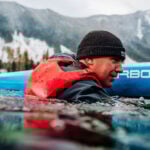 The Mustang Life Jacket Reinventing The Inflatable PFD man immersed in water beside his paddleboard while wearing a Mustang Khimera inflatable PFD