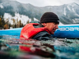 man immersed in water beside his paddleboard while wearing a Mustang Khimera inflatable PFD