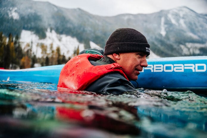 man immersed in water beside his paddleboard while wearing a Mustang Khimera inflatable PFD