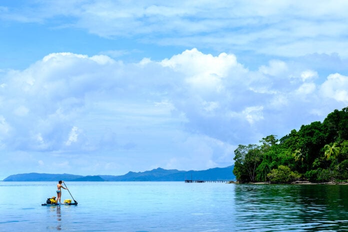 a woman paddleboards in an idyllic tropical location in Indonesia