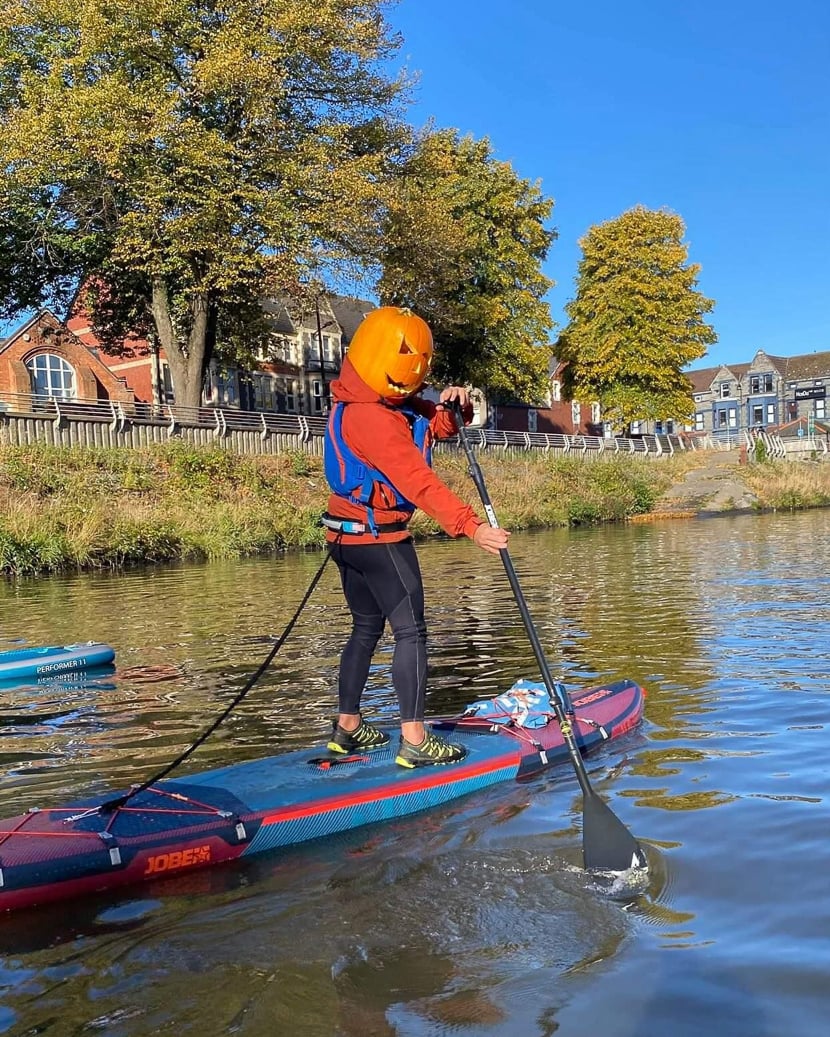 A person with a pumpkin on their head on a Stand Up Paddle Board