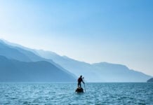 man stands and paddleboards on ocean waters with misty mountains in the background