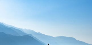 man stands and paddleboards on ocean waters with misty mountains in the background