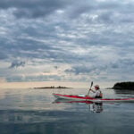 Best Touring Kayaks For 2026 woman paddles the Current Designs Karla touring kayak on a calm, somewhat cloudy day