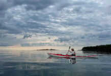 woman paddles the Current Designs Karla touring kayak on a calm, somewhat cloudy day