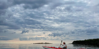 woman paddles the Current Designs Karla touring kayak on a calm, somewhat cloudy day