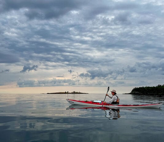 woman paddles the Current Designs Karla touring kayak on a calm, somewhat cloudy day