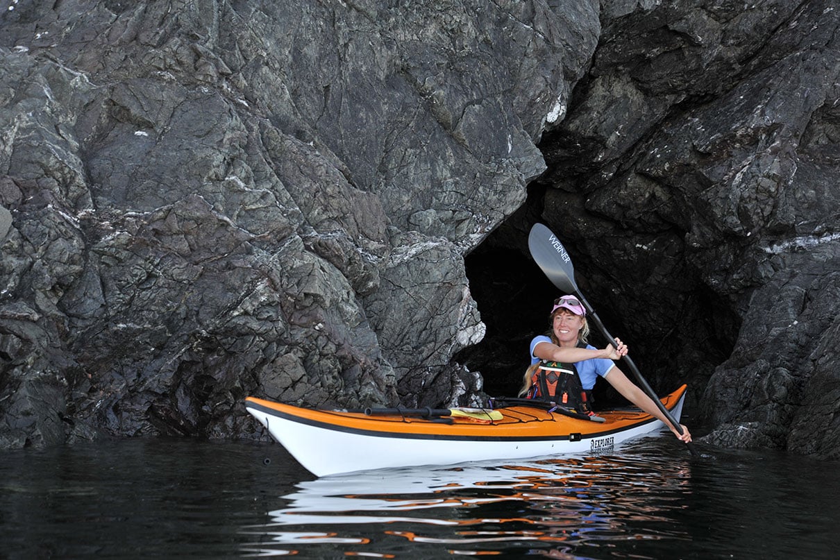 woman paddles the Nigel Dennis Explorer touring kayak near a rock face