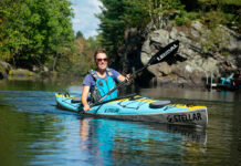 woman paddles the Stellar S14 G2 touring kayak near rocks and trees