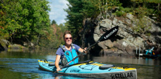 woman paddles the Stellar S14 G2 touring kayak near rocks and trees