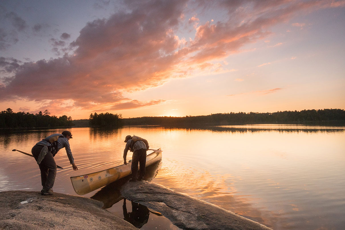 two people prepare to launch a canoe on calm lake at dawn