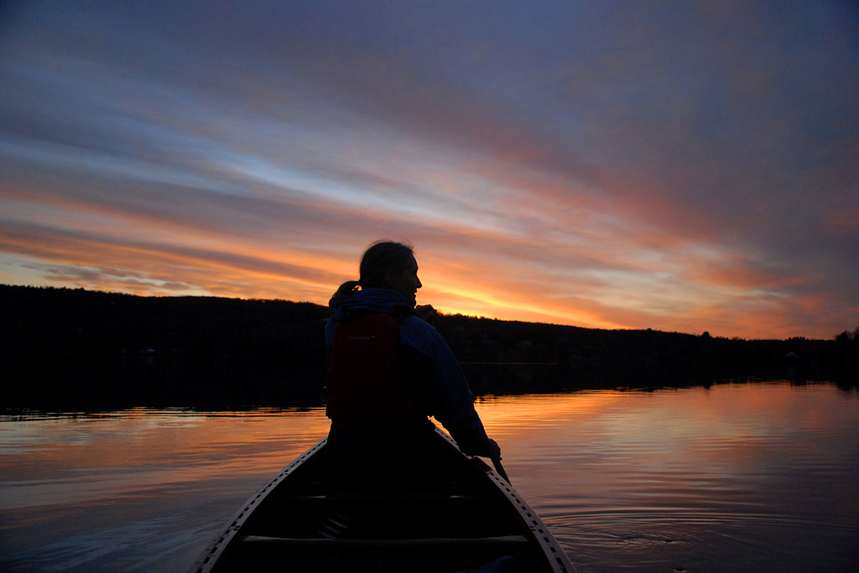 woman is silhouetted paddling a canoe at dusk