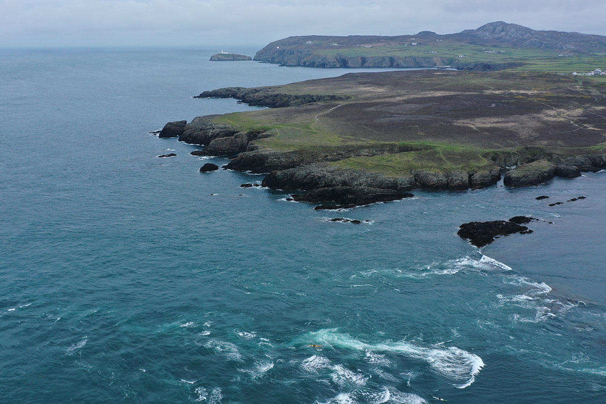 overhead view of a tiny person kayaking among swirling water off the coast of Wales