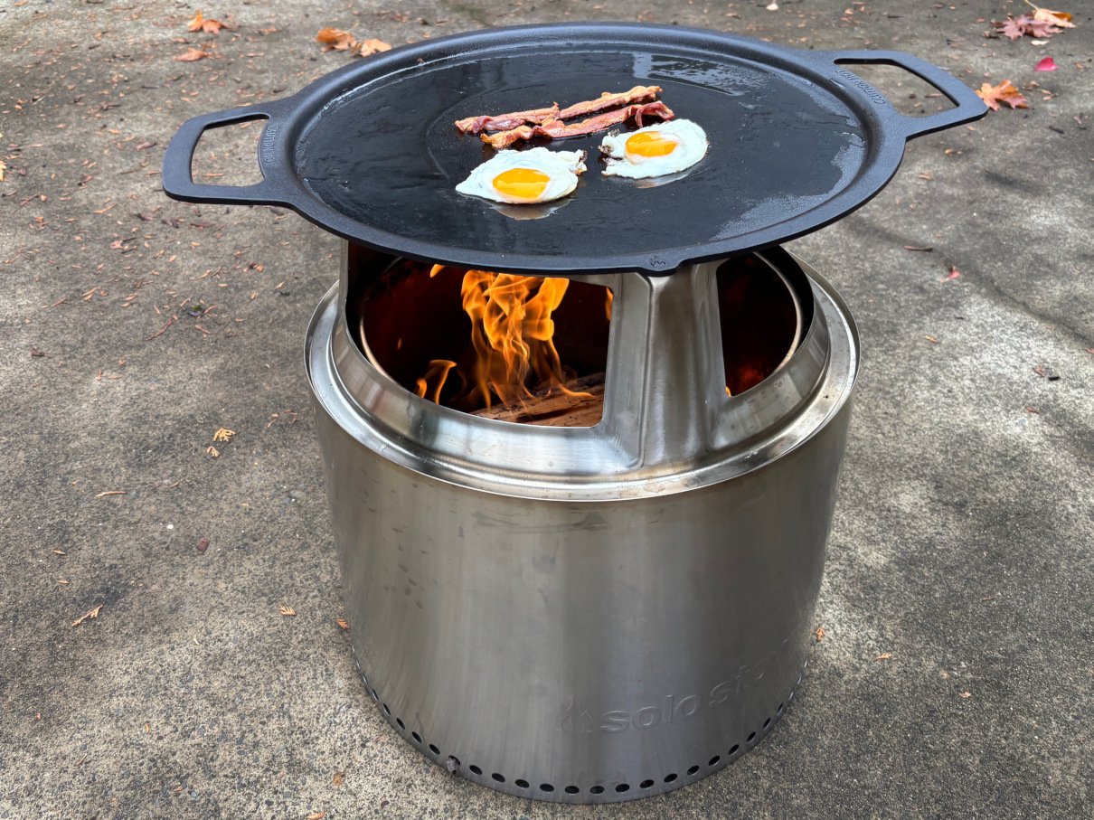 Eggs and bacon cooking on cast iron griddle over Solo Stove.