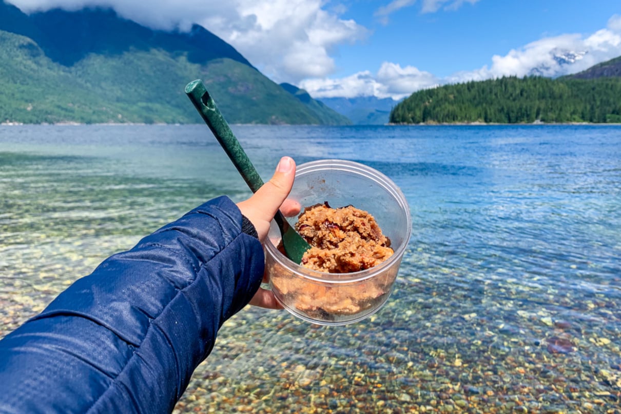 Bowl of food held out in view in front of clear lake.