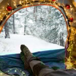 Best Camping Gifts a person lays in a cozy tent decorated with Christmas lights in winter