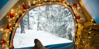 a person lays in a cozy tent decorated with Christmas lights in winter