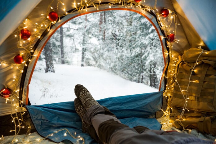 a person lays in a cozy tent decorated with Christmas lights in winter