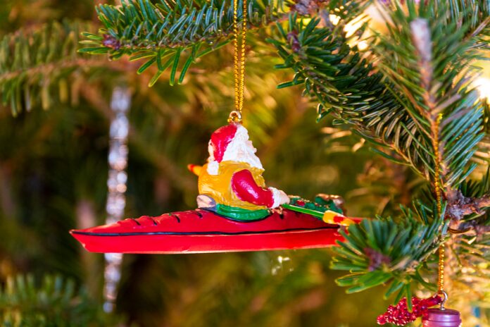 santa kayaking ornament on a christmas tree with gifts underneath