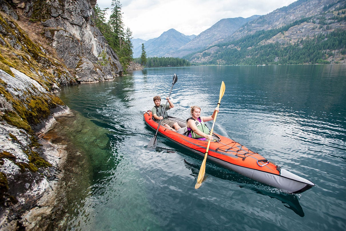 two people paddle the Advanced Elements AdvancedFrame Convertible Elite tandem inflatable kayak on scenic mountain lake