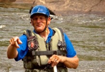 Charlie Walbridge, author of Whitewater Rescues, stands and points in a knee-deep river with rescue gear and paddle