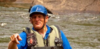 Charlie Walbridge, author of Whitewater Rescues, stands and points in a knee-deep river with rescue gear and paddle