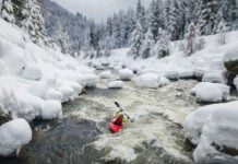 a person paddles down a river in a snowy winter landscape while wearing a drysuit that respects the upcoming PFAS ban