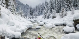 a person paddles down a river in a snowy winter landscape while wearing a drysuit that respects the upcoming PFAS ban