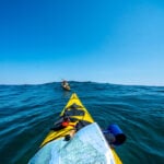 bow shot of a sea kayaker with map paddling after another kayaker over an ocean swell while they are on an expedition