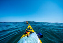 bow shot of a sea kayaker with map paddling after another kayaker over an ocean swell while they are on an expedition