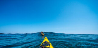 bow shot of a sea kayaker with map paddling after another kayaker over an ocean swell while they are on an expedition