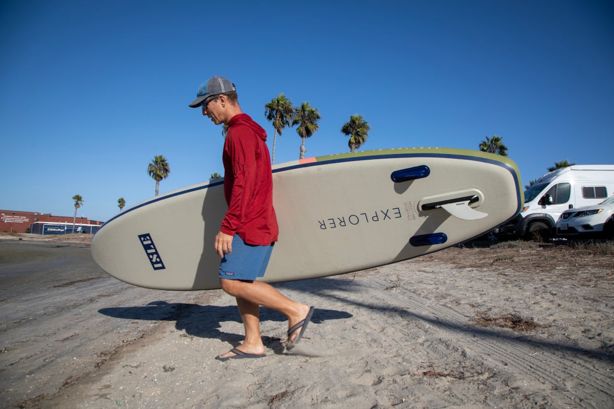 Man walking paddleboard to the water in San Diego.