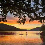two people paddleboarding while silhouetted by the sunset at Loch Lomond, Scotland