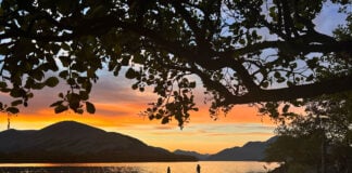 two people paddleboarding while silhouetted by the sunset at Loch Lomond, Scotland