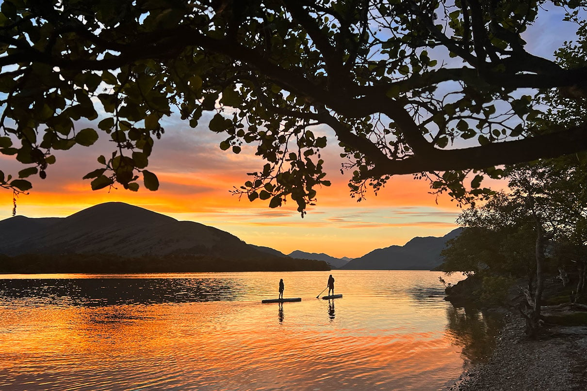 two people paddleboarding while silhouetted by the sunset at Loch Lomond, Scotland