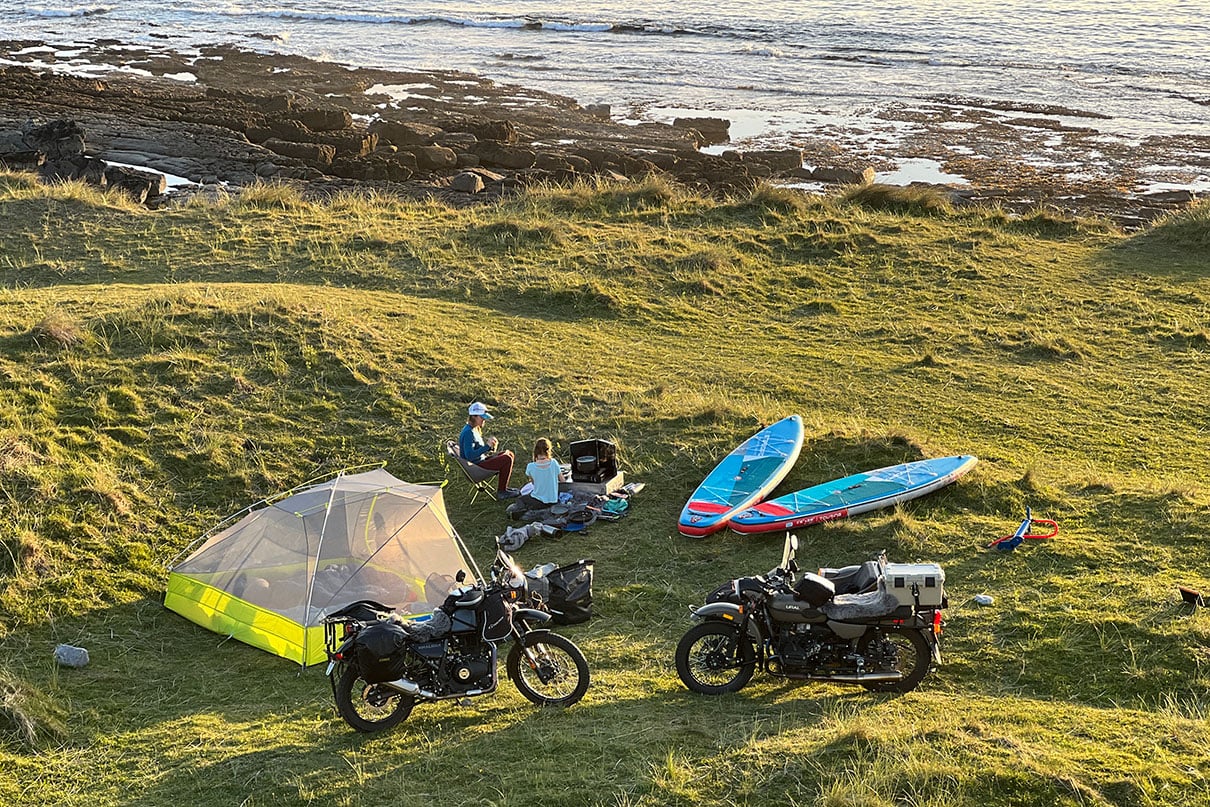 the Lawson's family motorcycles parked by their campsite with paddleboards along the grassy coast near Galway, Ireland