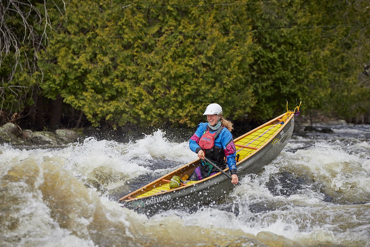 Stefi van Wijk smiles while paddling an open canoe with whitewater outfitting through rapids on the Madawaska River