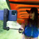 woman smiles at her phone held on a selfie stick while portaging a canoe