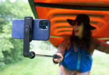 woman smiles at her phone held on a selfie stick while portaging a canoe