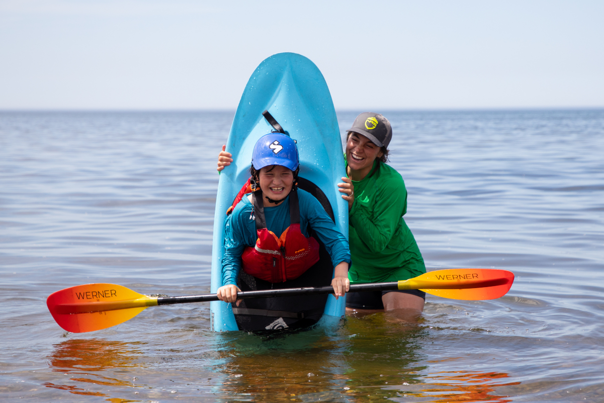 Woman standing in water teaching child how to kayak.