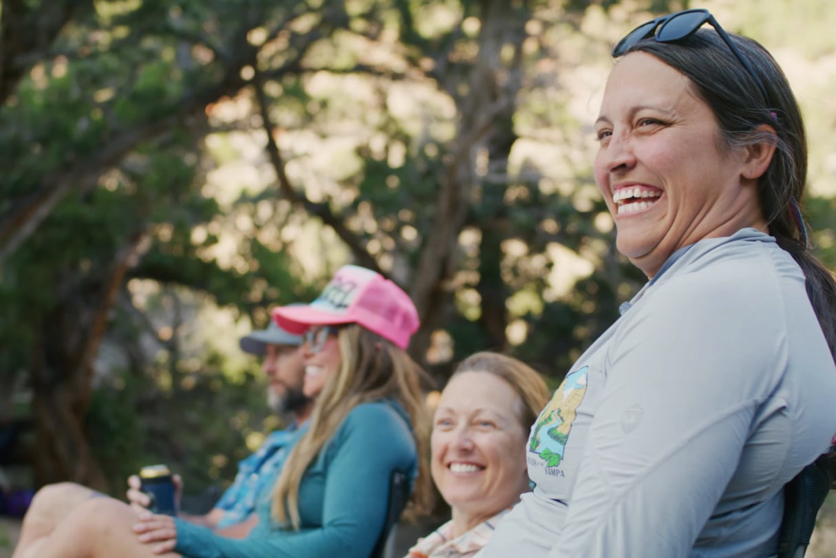 Women smiling as they sit around their river camp.