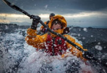 two people paddle through surf while wearing drysuits