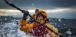 two people paddle through surf while wearing drysuits