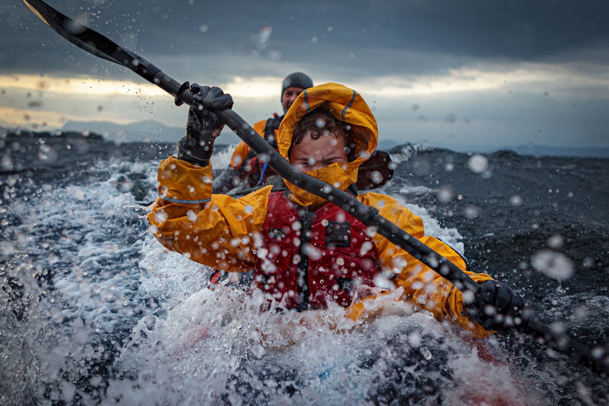 two people paddle through surf while wearing drysuits