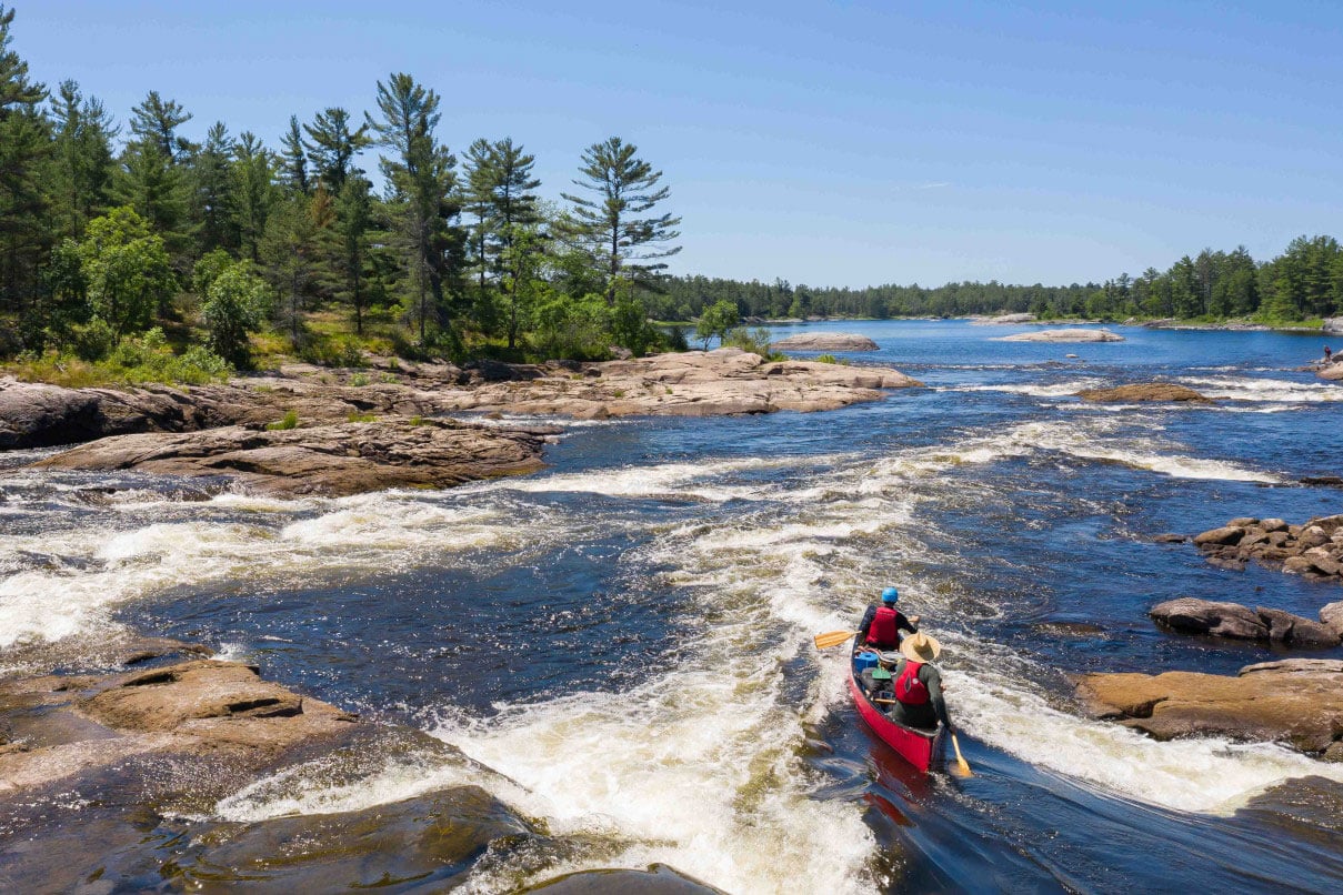 two people canoe through a set of Class II rapids